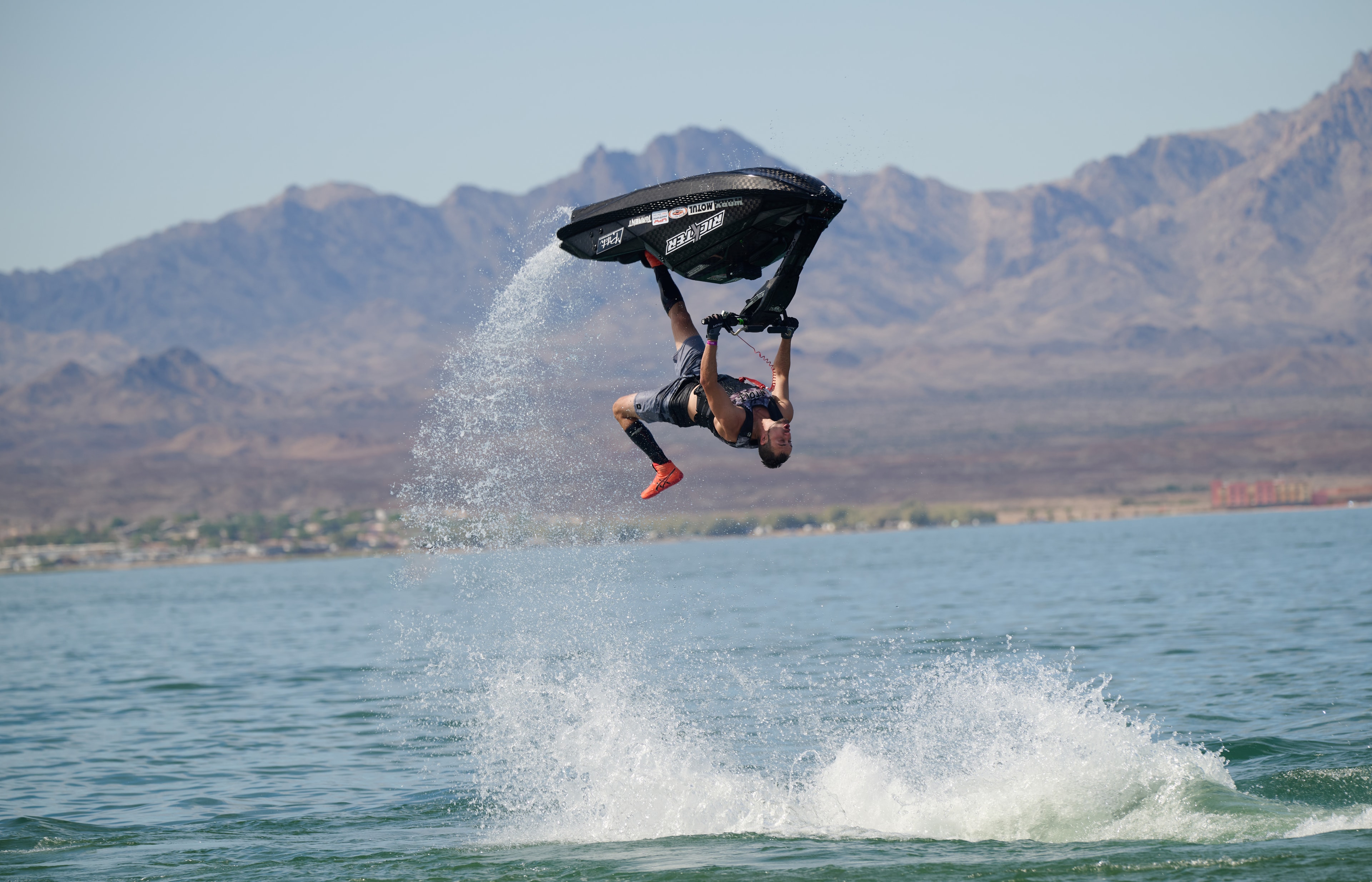 Action sports — jetski rider fully inverted mid-air with mountain backdrop