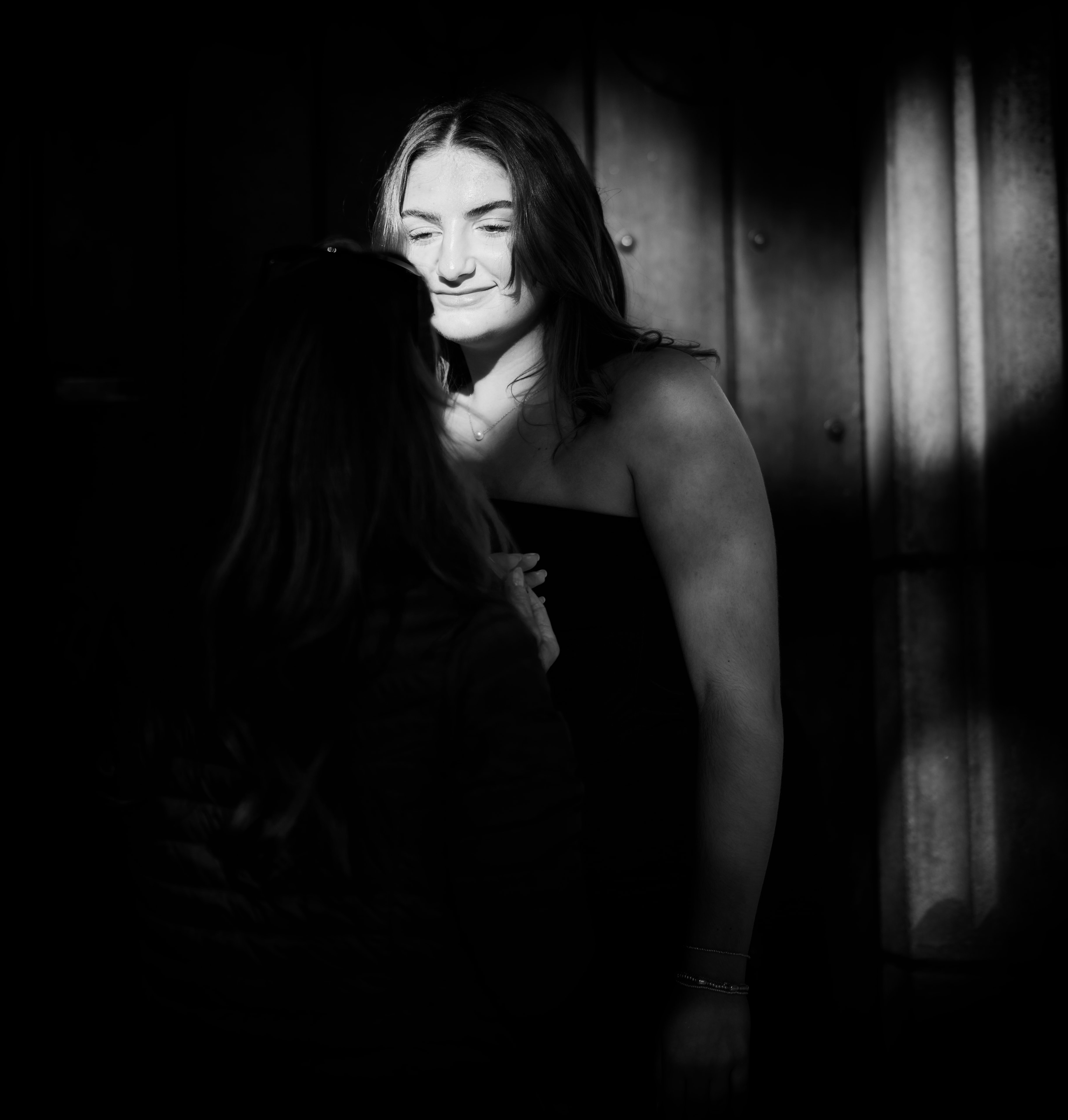 Senior portrait — dramatic black and white, young woman in soft light against barn door